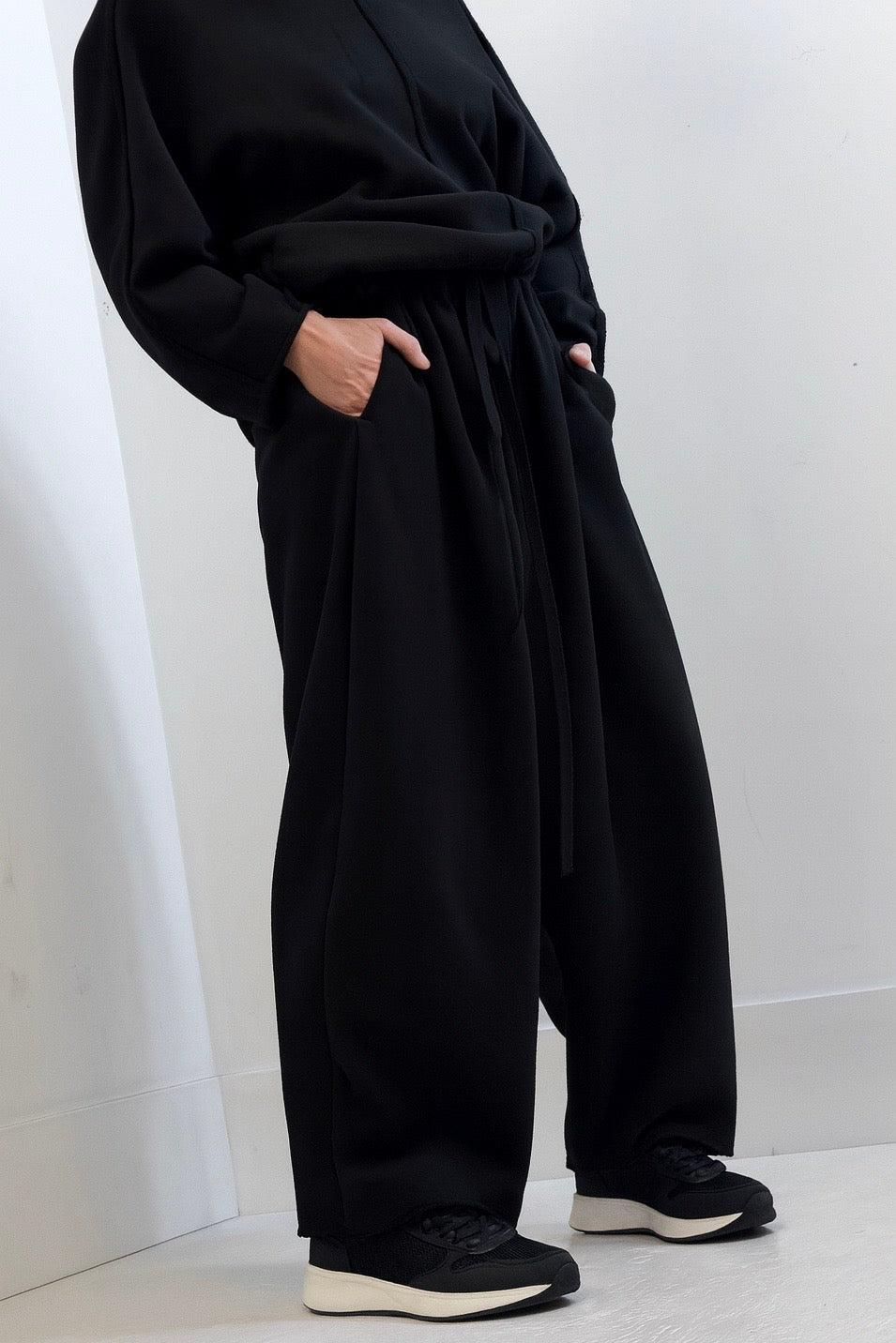 Person wearing a loose-fitting black outfit with wide-leg pants against a white background