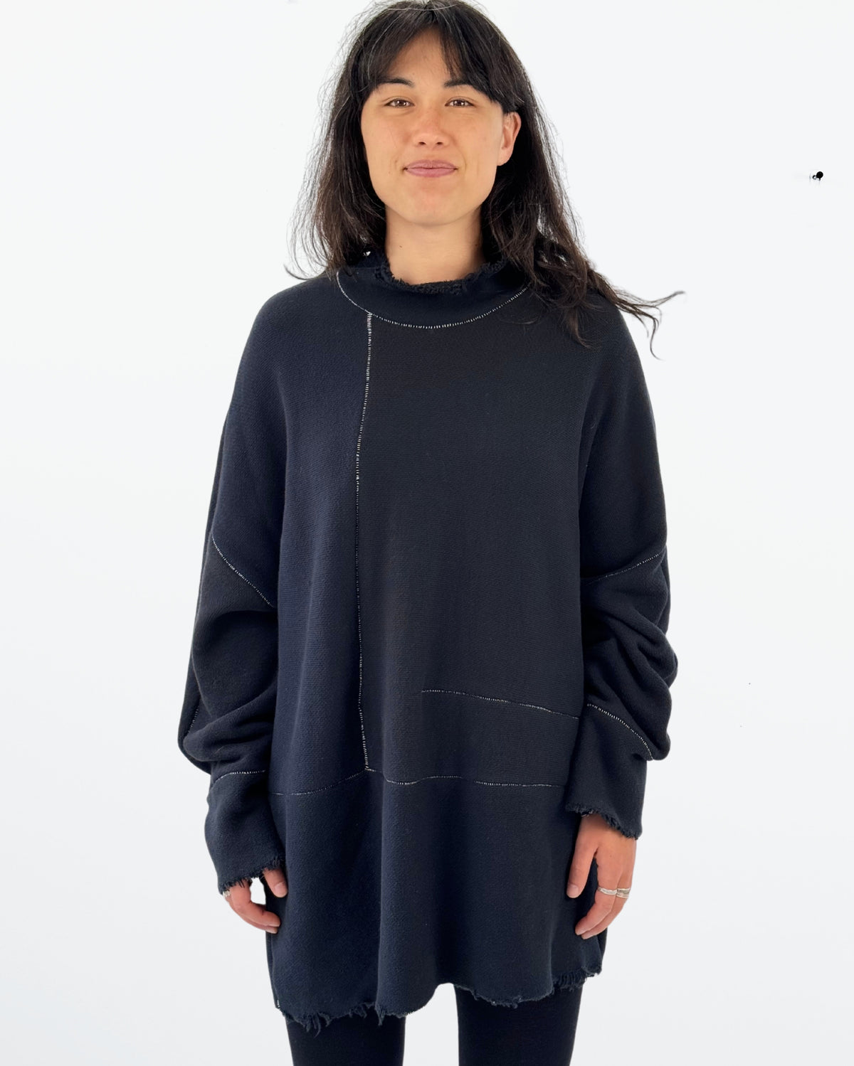 A person wearing a navy-colored oversized pullover with open seam detailing and raw edges at the neck, sleeves, and hem.