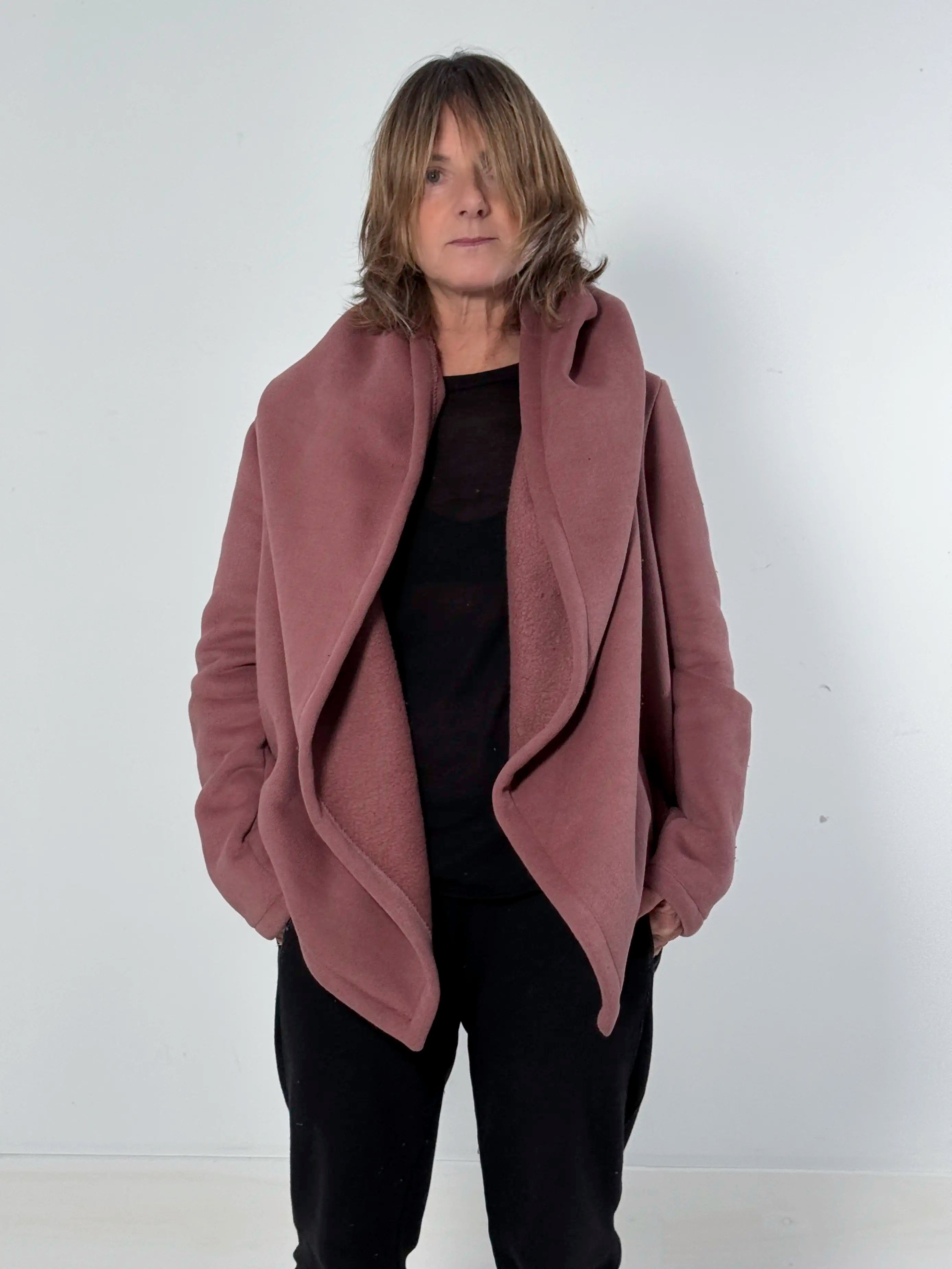 Person wearing a mauve coat over a black top and pants on a white background