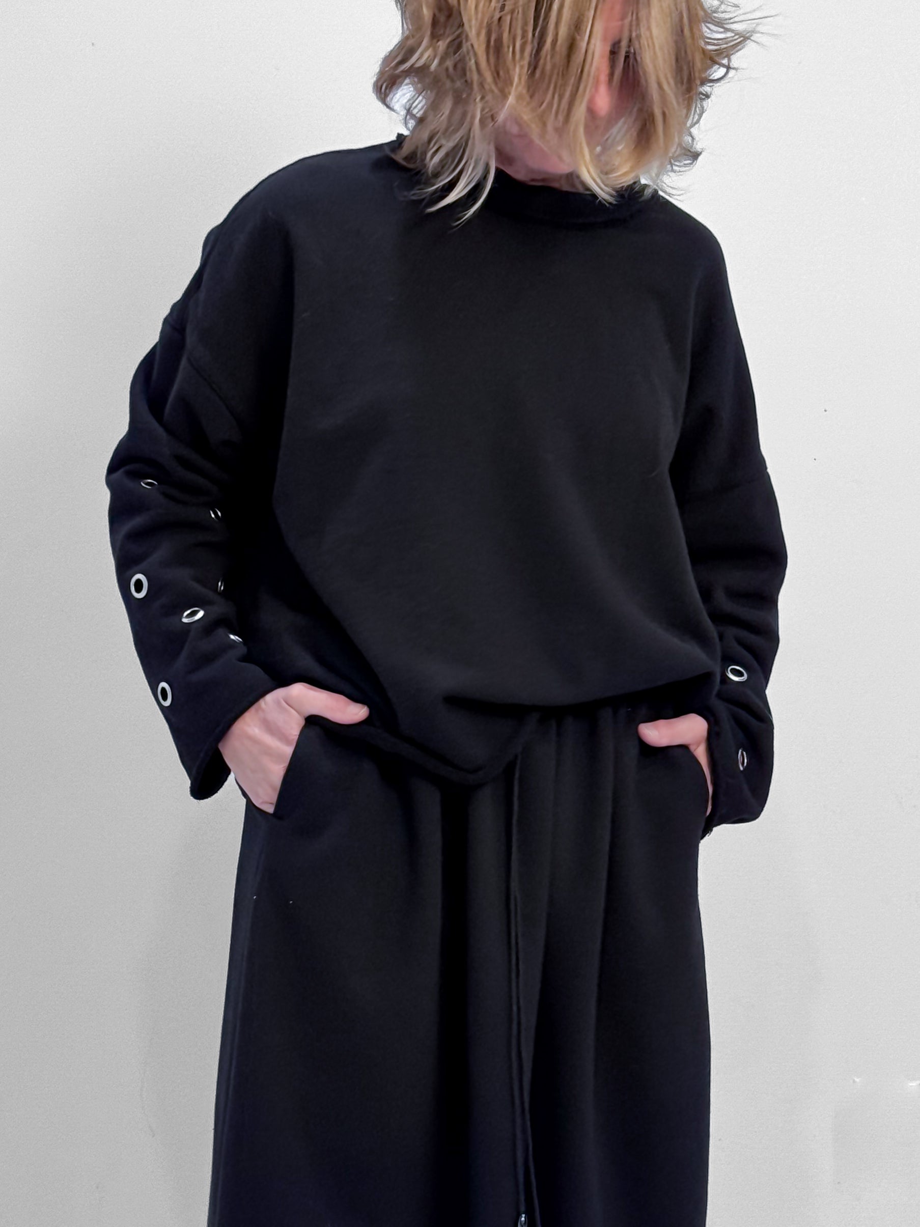 Person wearing a black outfit with grommet details on a plain background