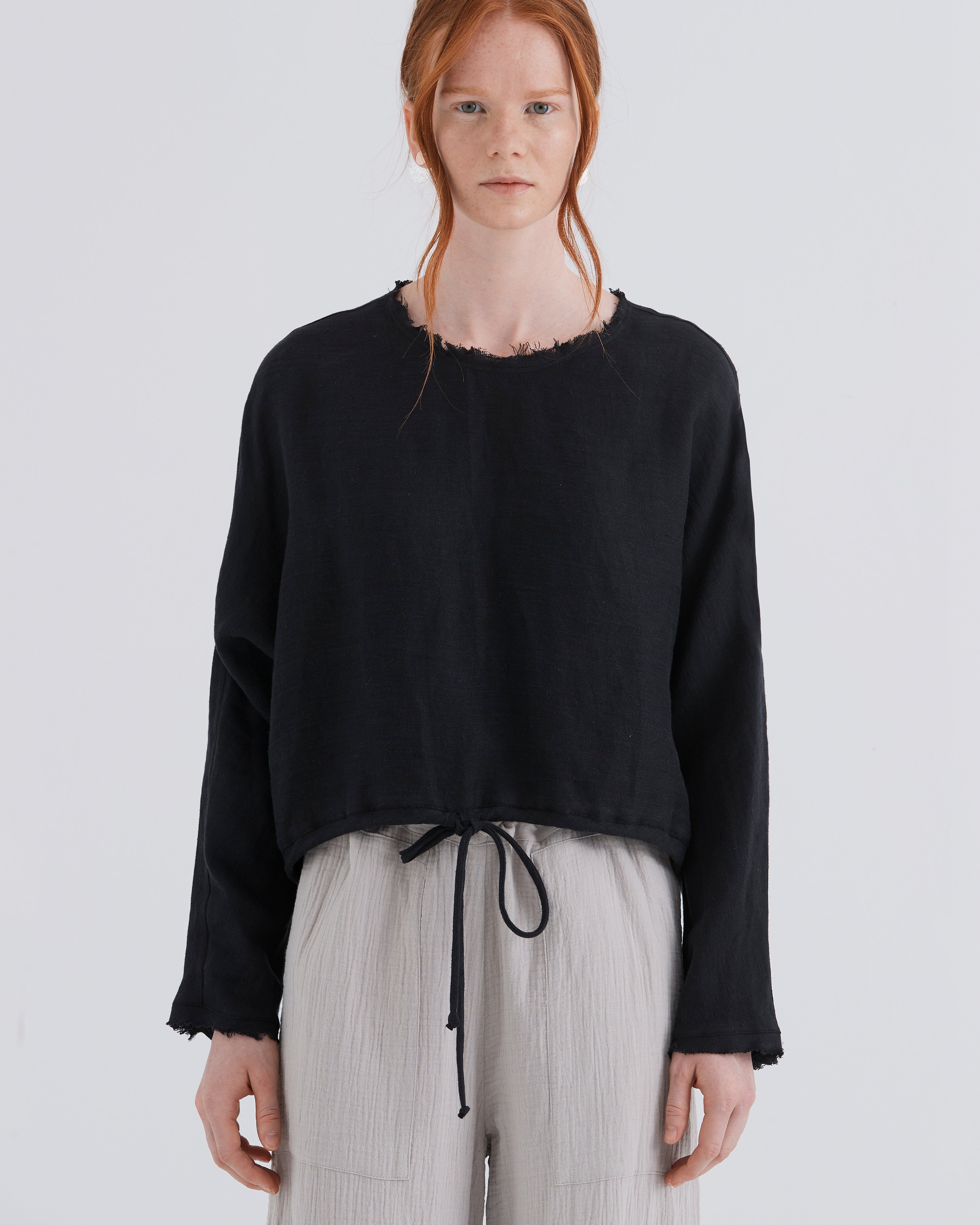 Person wearing a black sweater and light gray pants on a white background