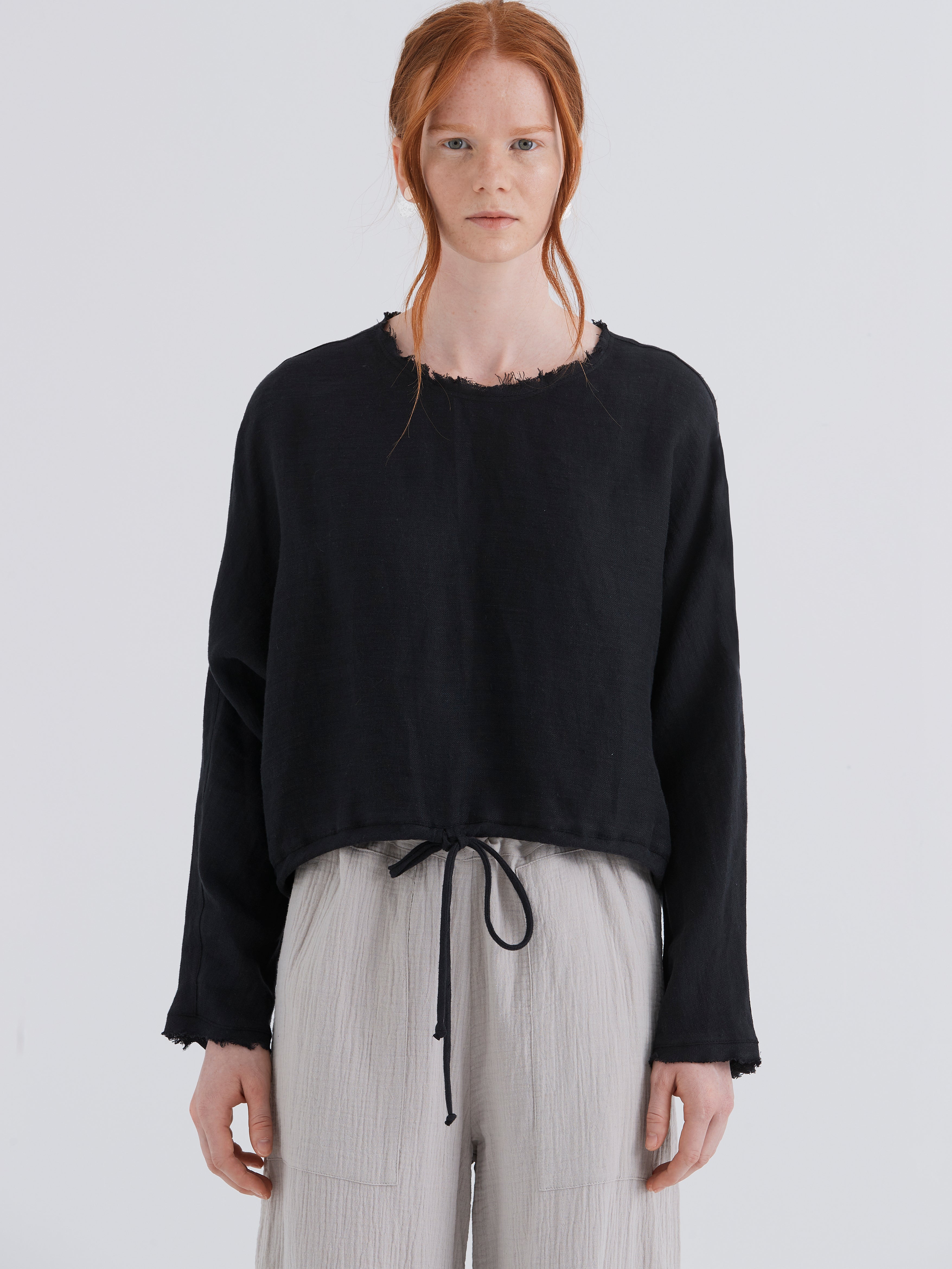 Person wearing a black sweater and light gray pants on a white background