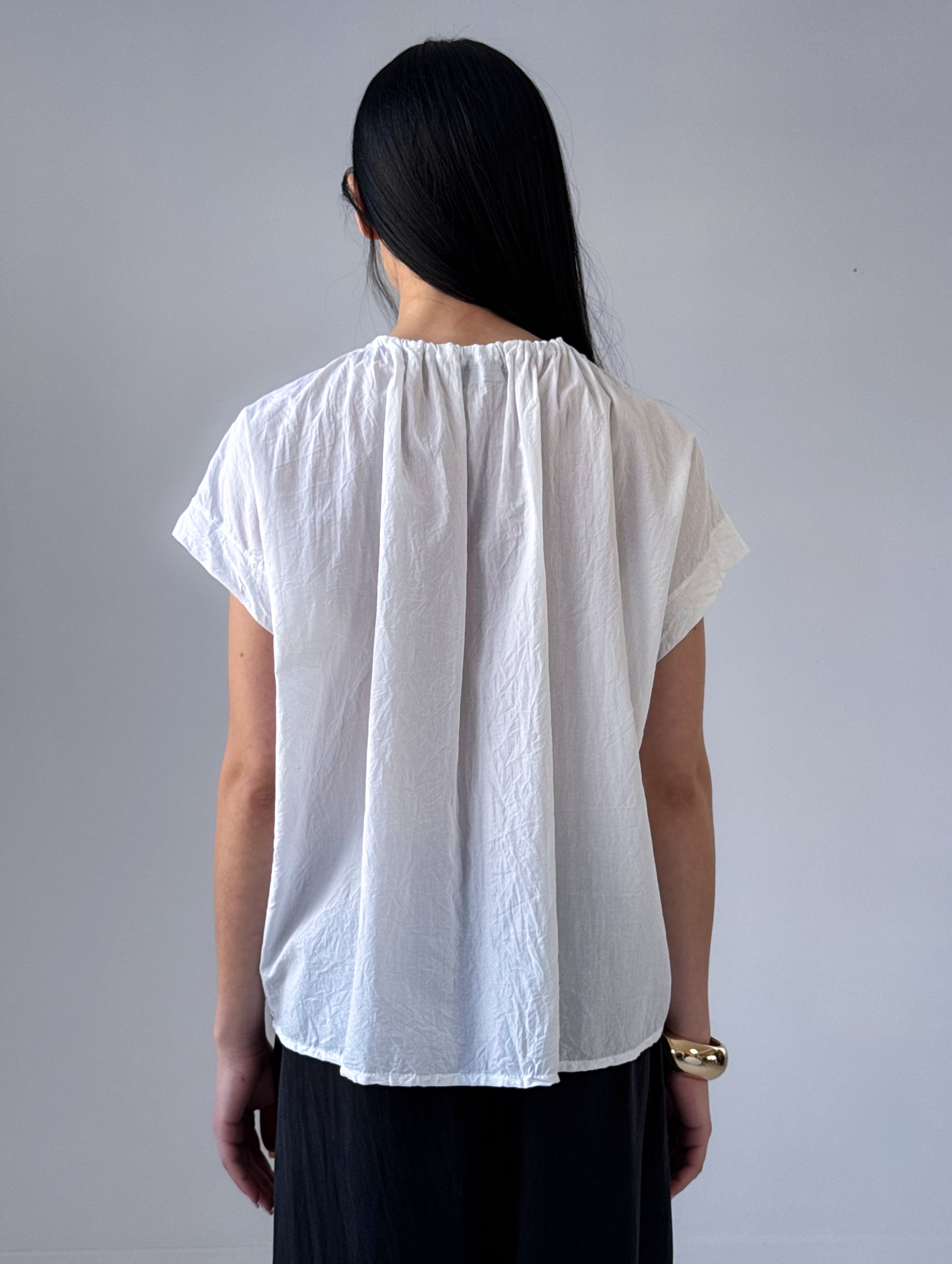 Person wearing a white blouse with short sleeves against a gray background