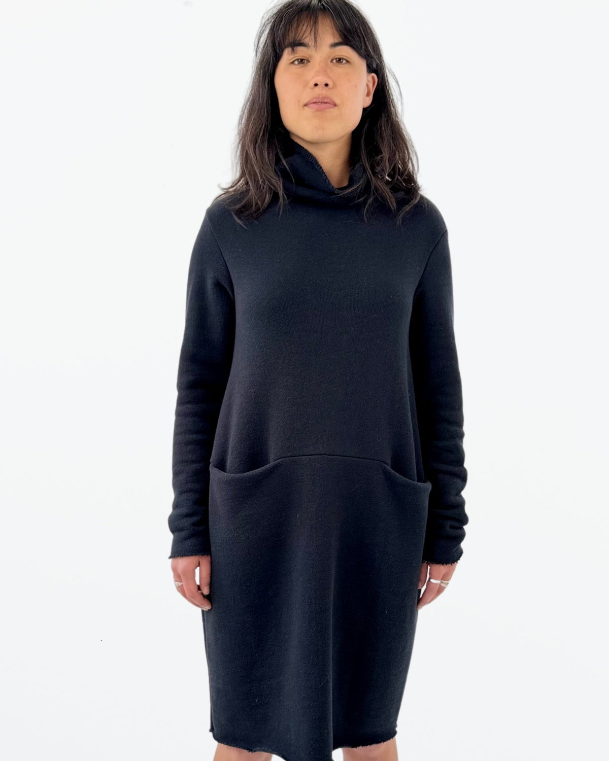 A woman wearing a navy long sleeve dress with a funnel neck and front pockets.