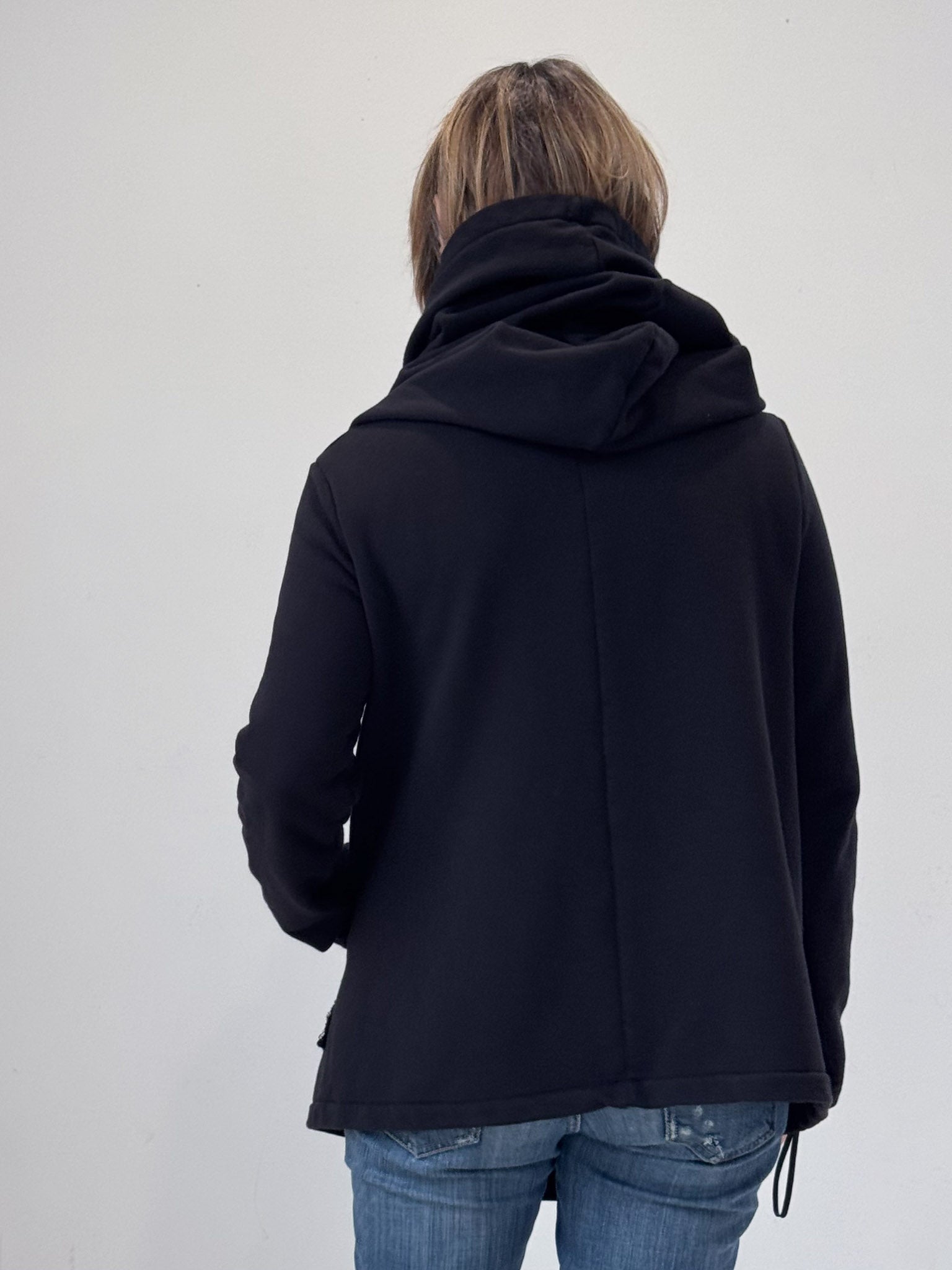 Person wearing a black jacket with a hood on a plain background