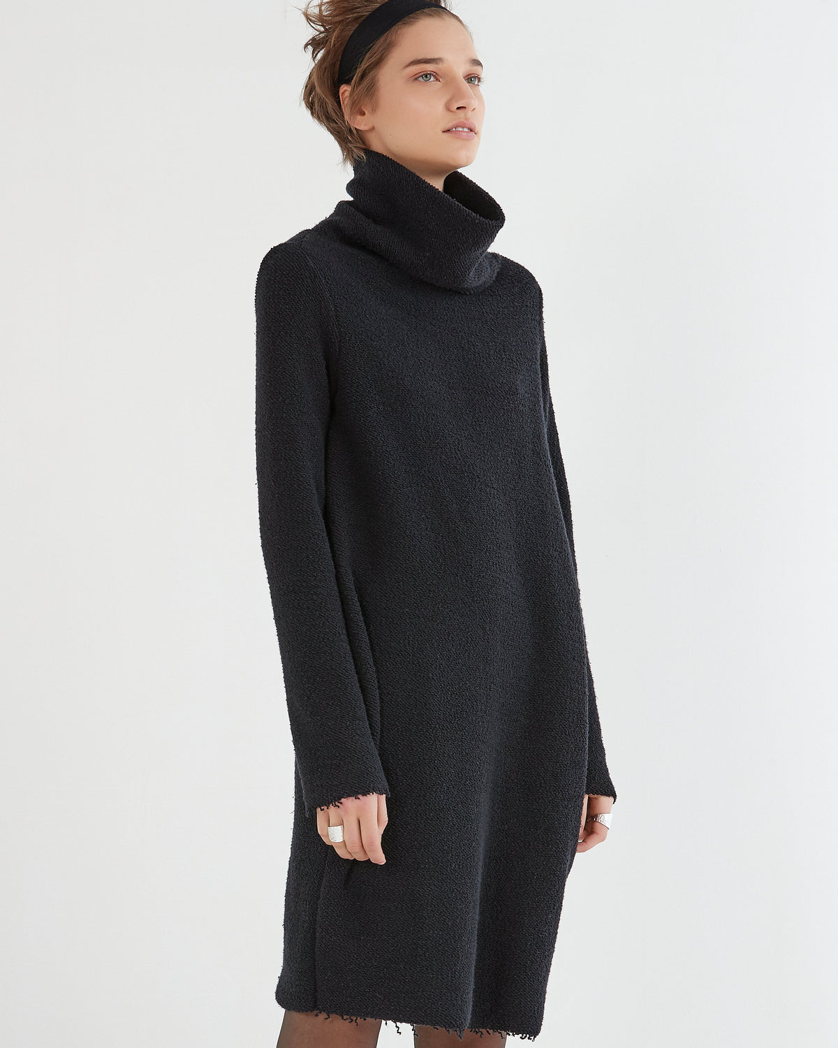 A model wearing a black, loosely draped pullover dress with a large neckline and long sleeves.