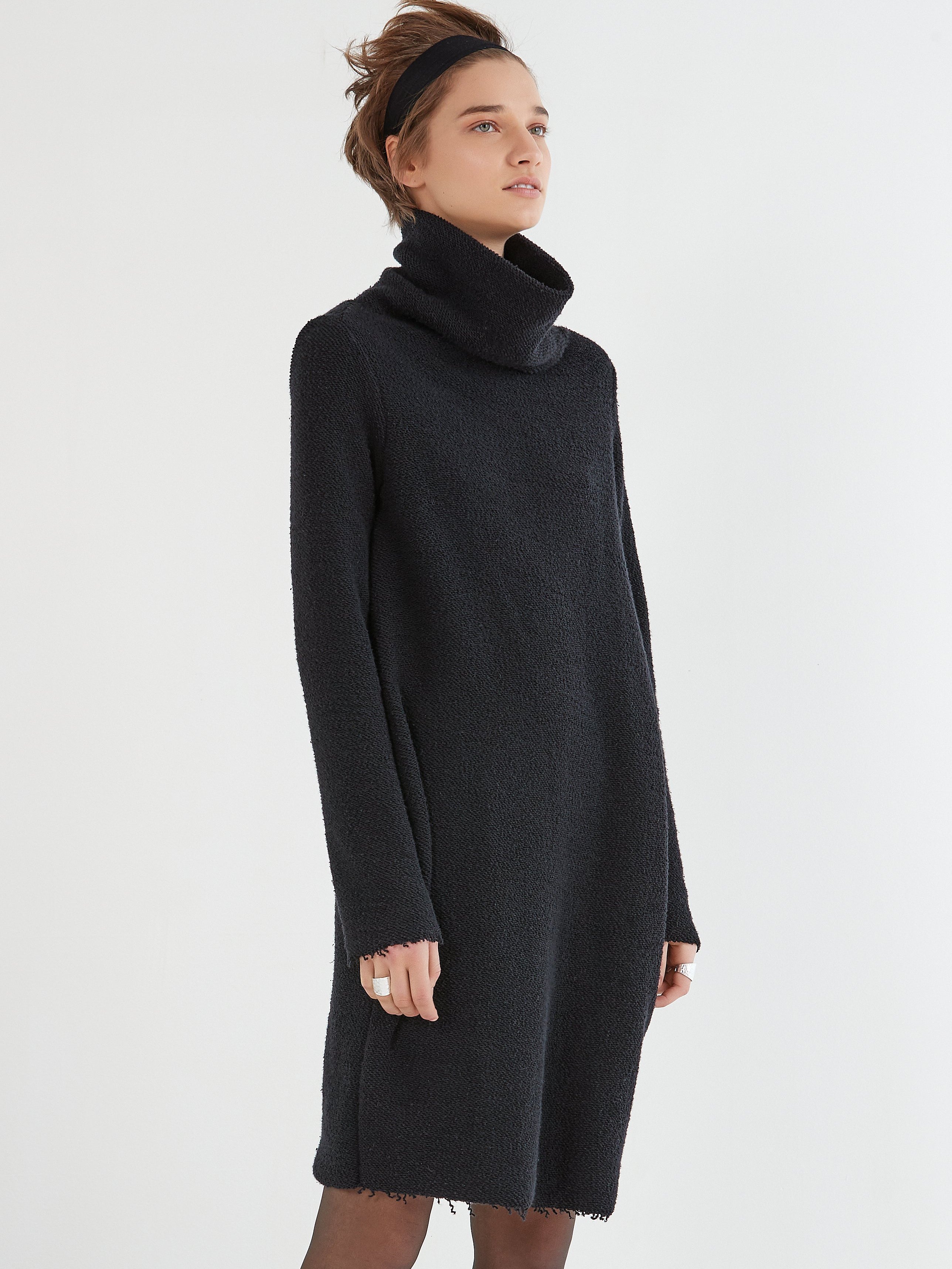 A model wearing a black, loosely draped pullover dress with a large neckline and long sleeves.