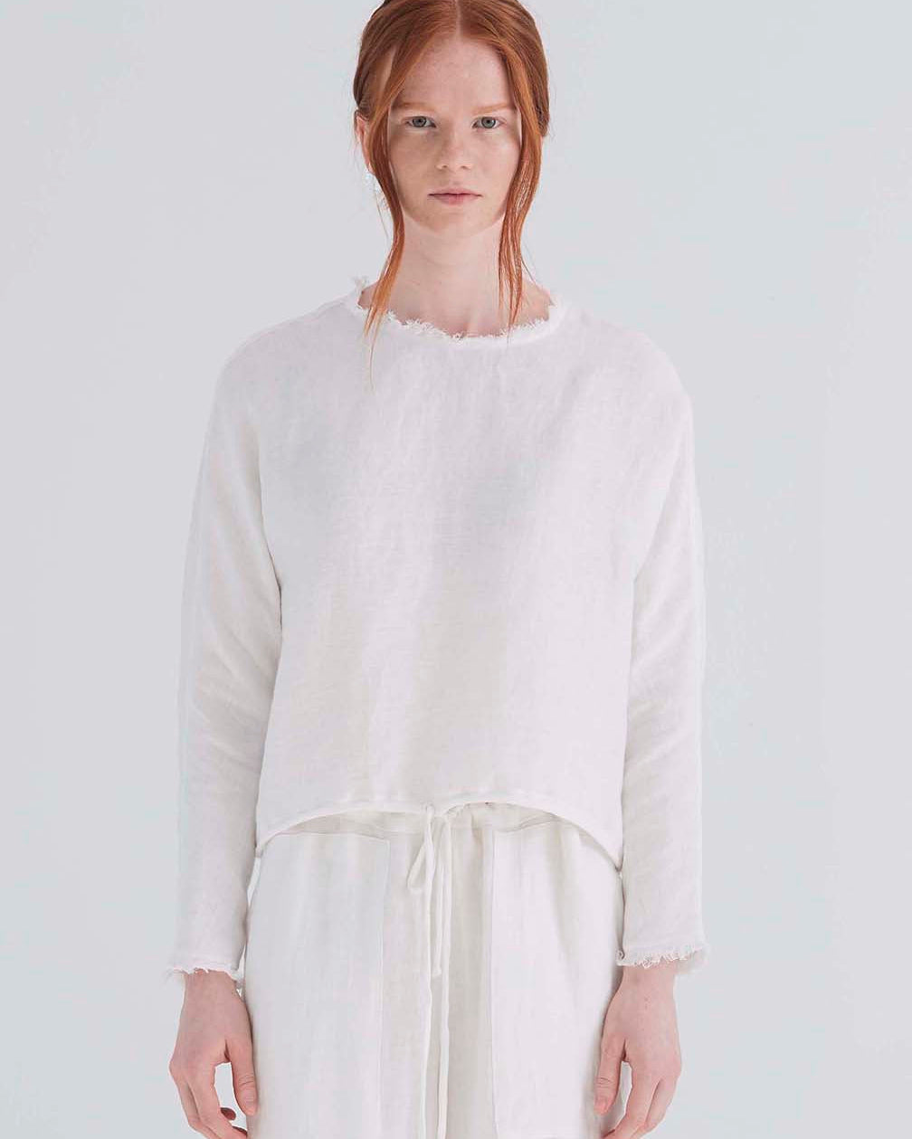 A woman wearing an oversized cropped white top with dolman sleeves and a drawstring hemline.