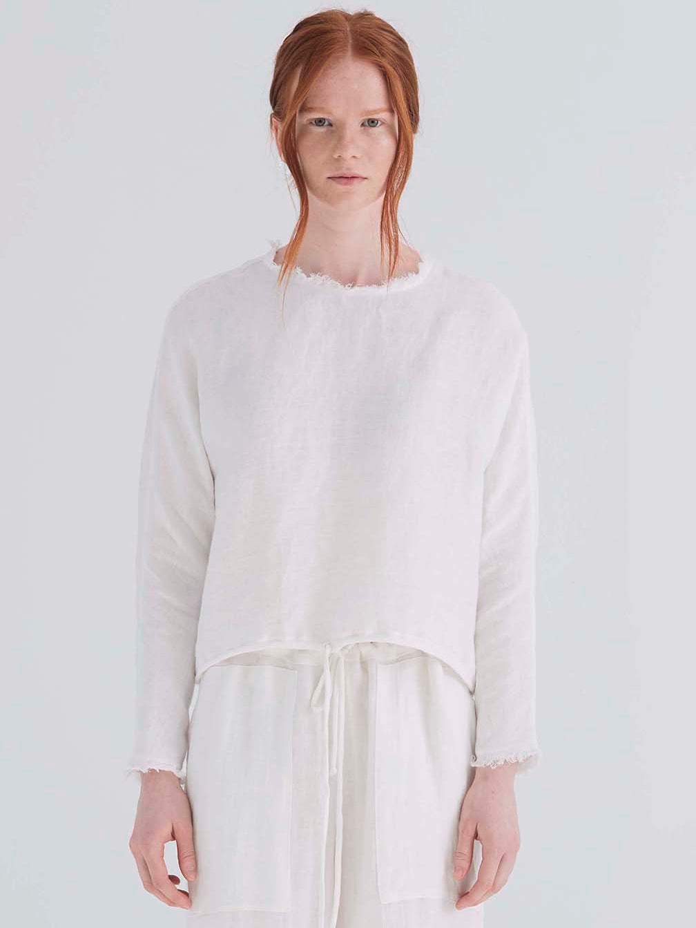 A woman wearing an oversized cropped white top with dolman sleeves and a drawstring hemline.
