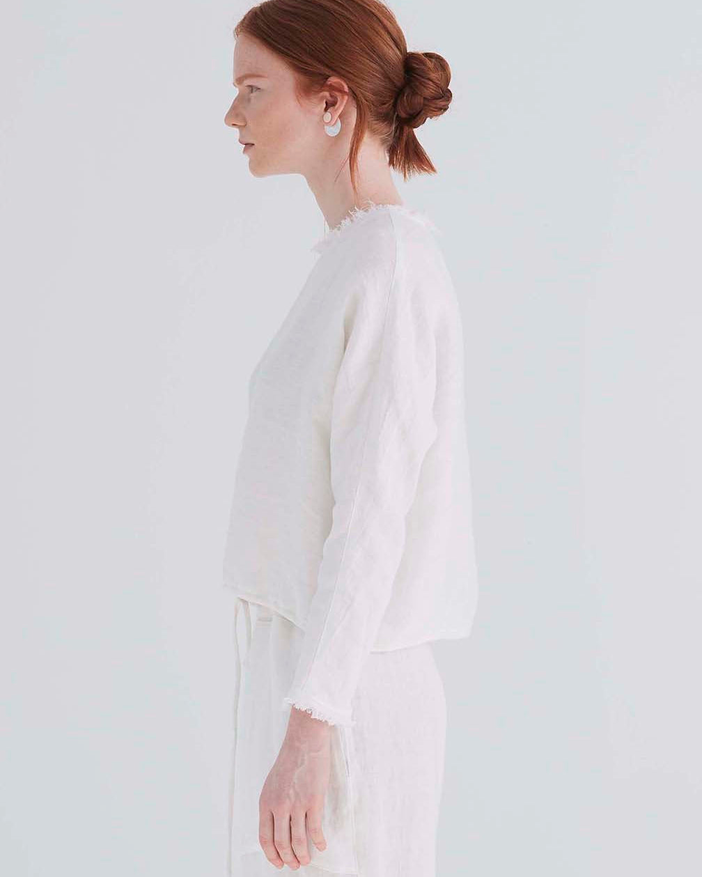 side view of a woman wearing an oversized cropped white top with dolman sleeves and a drawstring hemline.