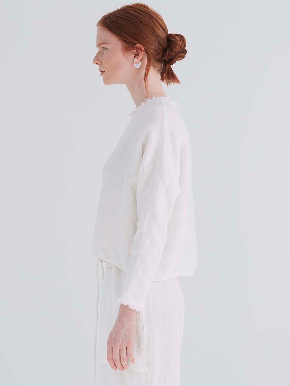 side view of a woman wearing an oversized cropped white top with dolman sleeves and a drawstring hemline.