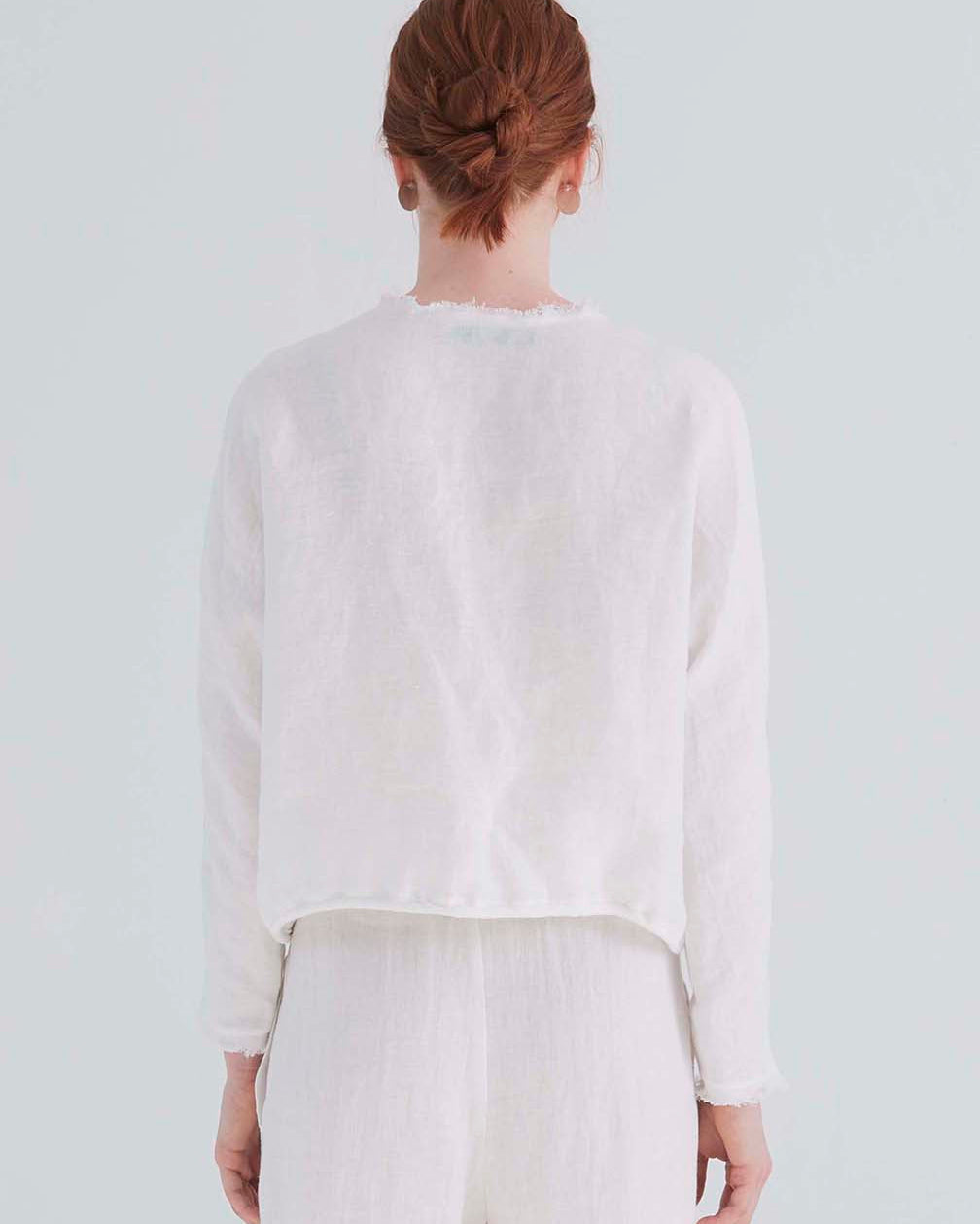 back view of a woman wearing an oversized cropped white top with dolman sleeves and a drawstring hemline.