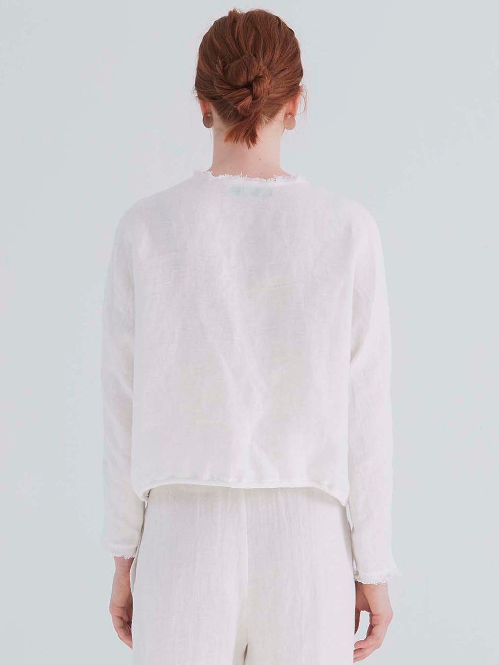back view of a woman wearing an oversized cropped white top with dolman sleeves and a drawstring hemline.