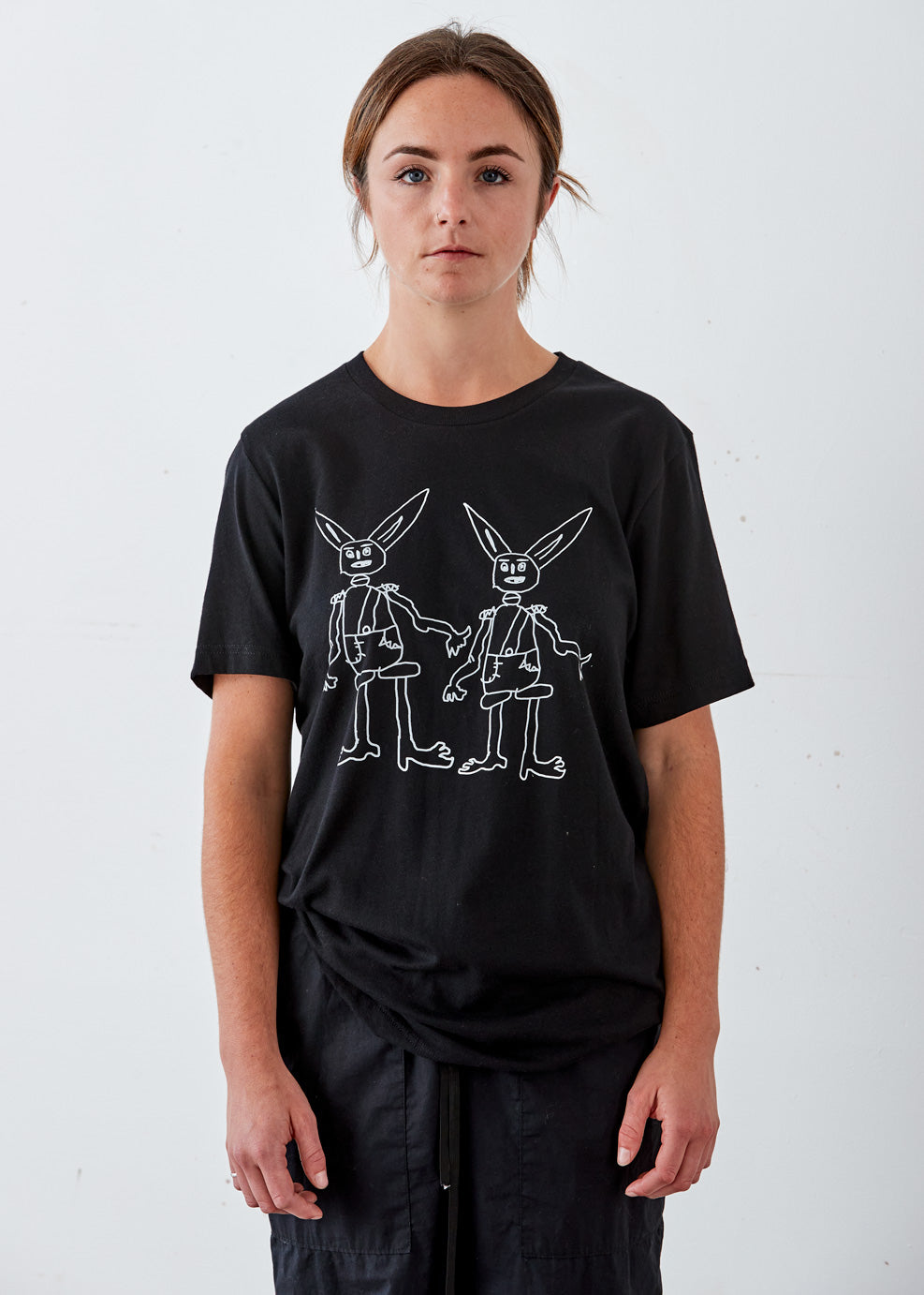 A person wearing a black crew neck t-shirt with a white graphic of two stylized rabbits.