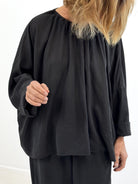 Person wearing a black long-sleeve top with a plain background