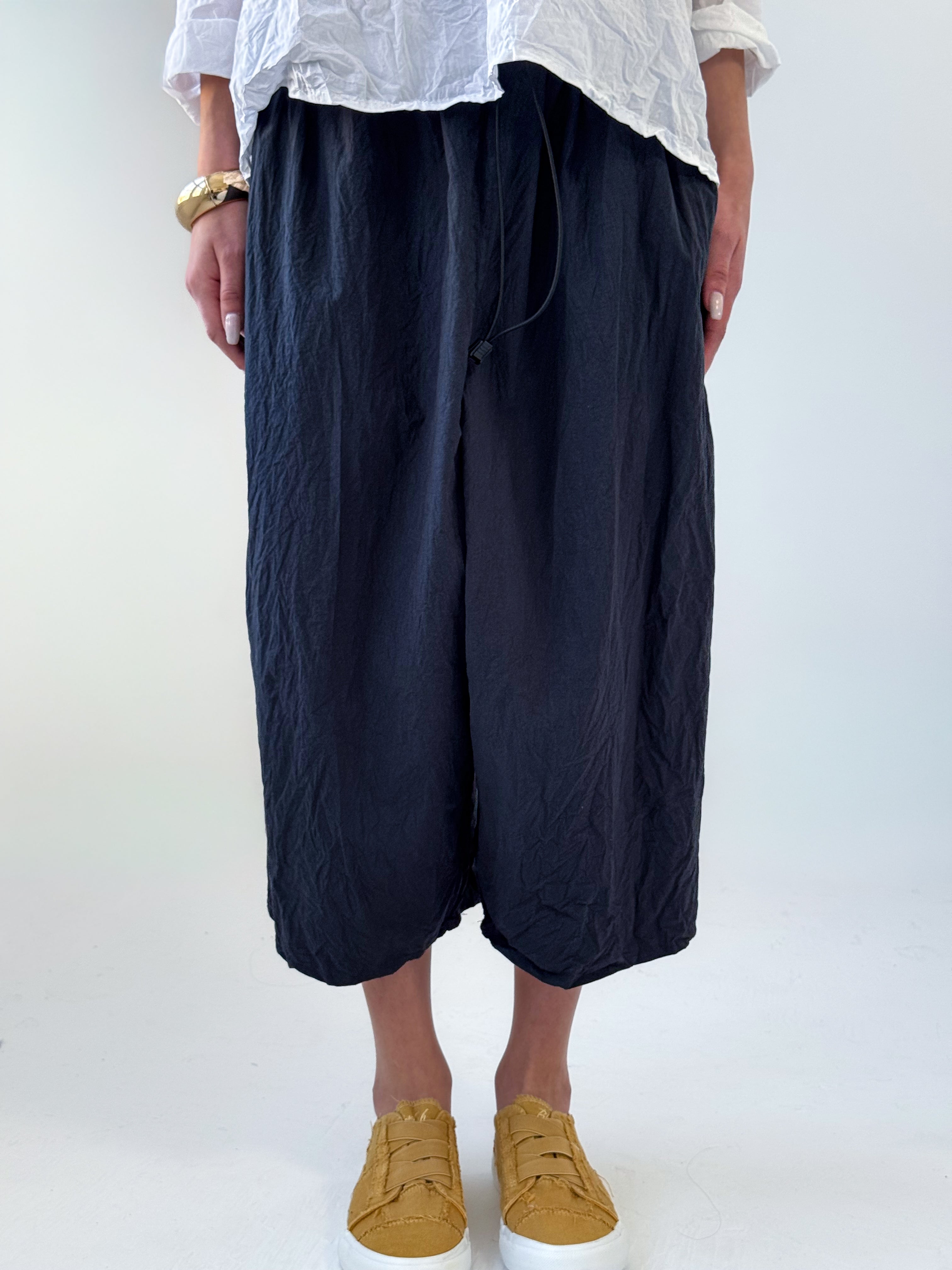 Noor drop crotch pants in crumpled black cotton with drawstring waist and relaxed cropped silhouette