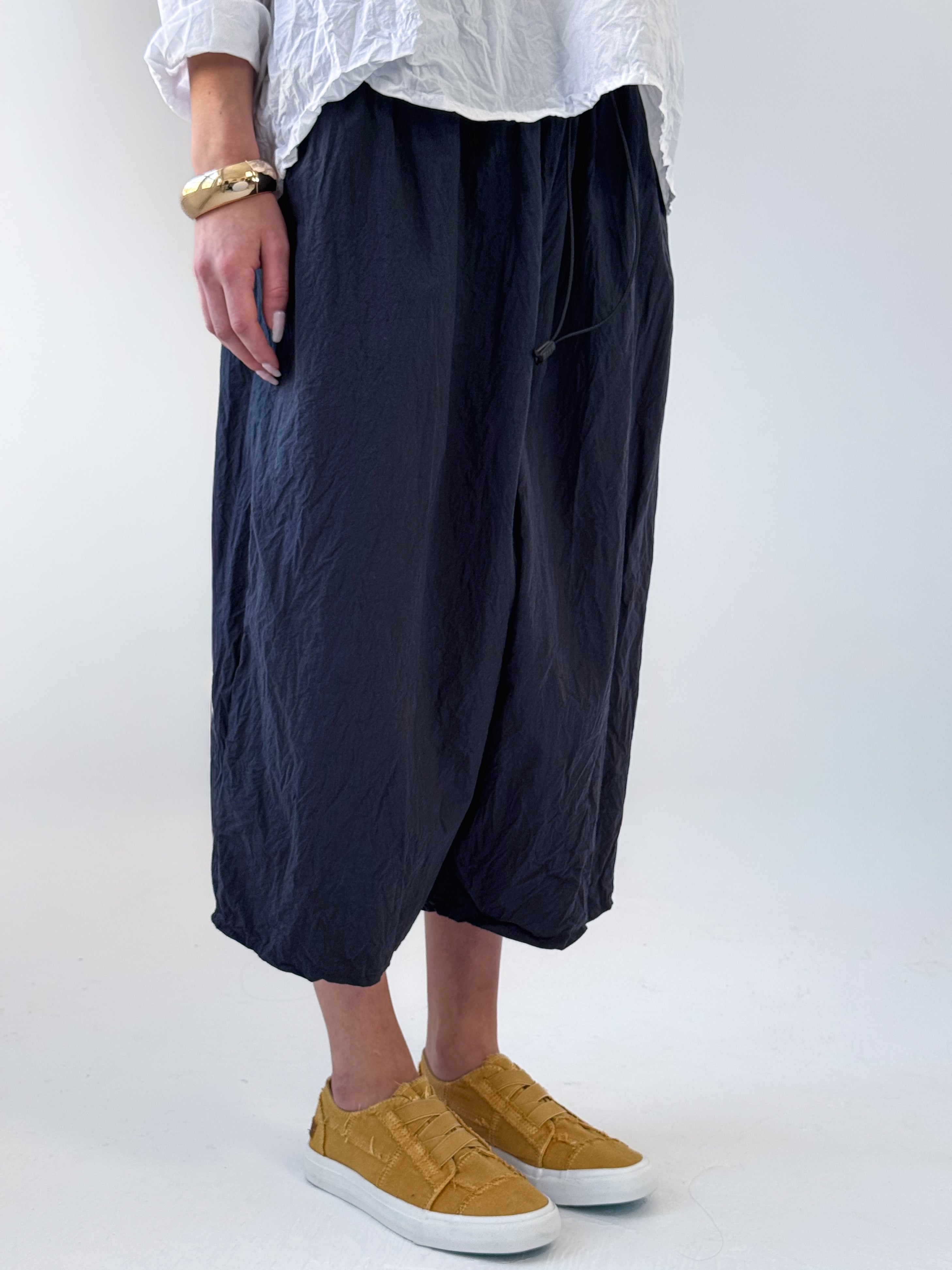 Noor drop crotch pants in crumpled black cotton with drawstring waist and relaxed cropped silhouette