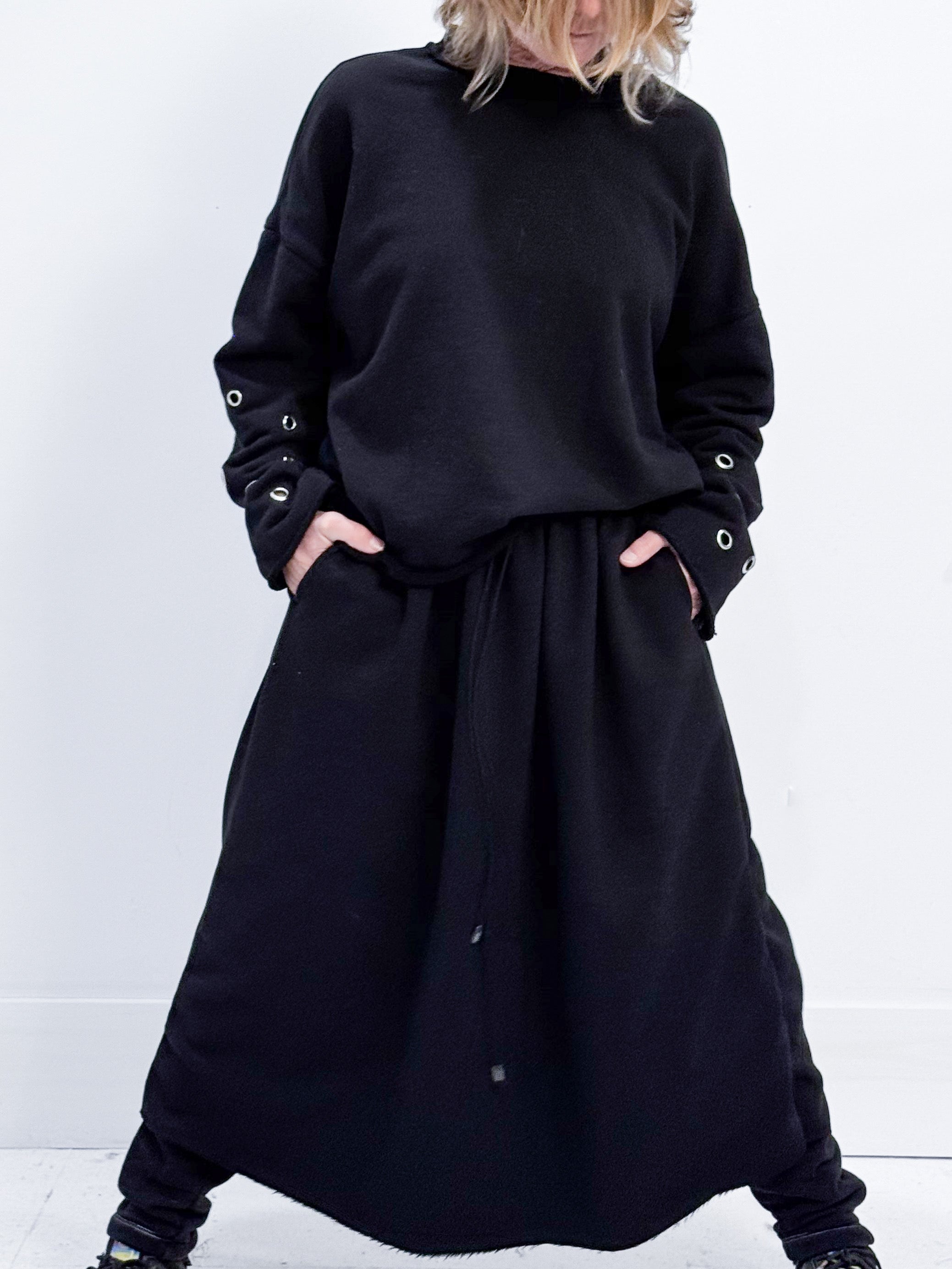 Person wearing a black outfit with a long dress and sweater against a white background