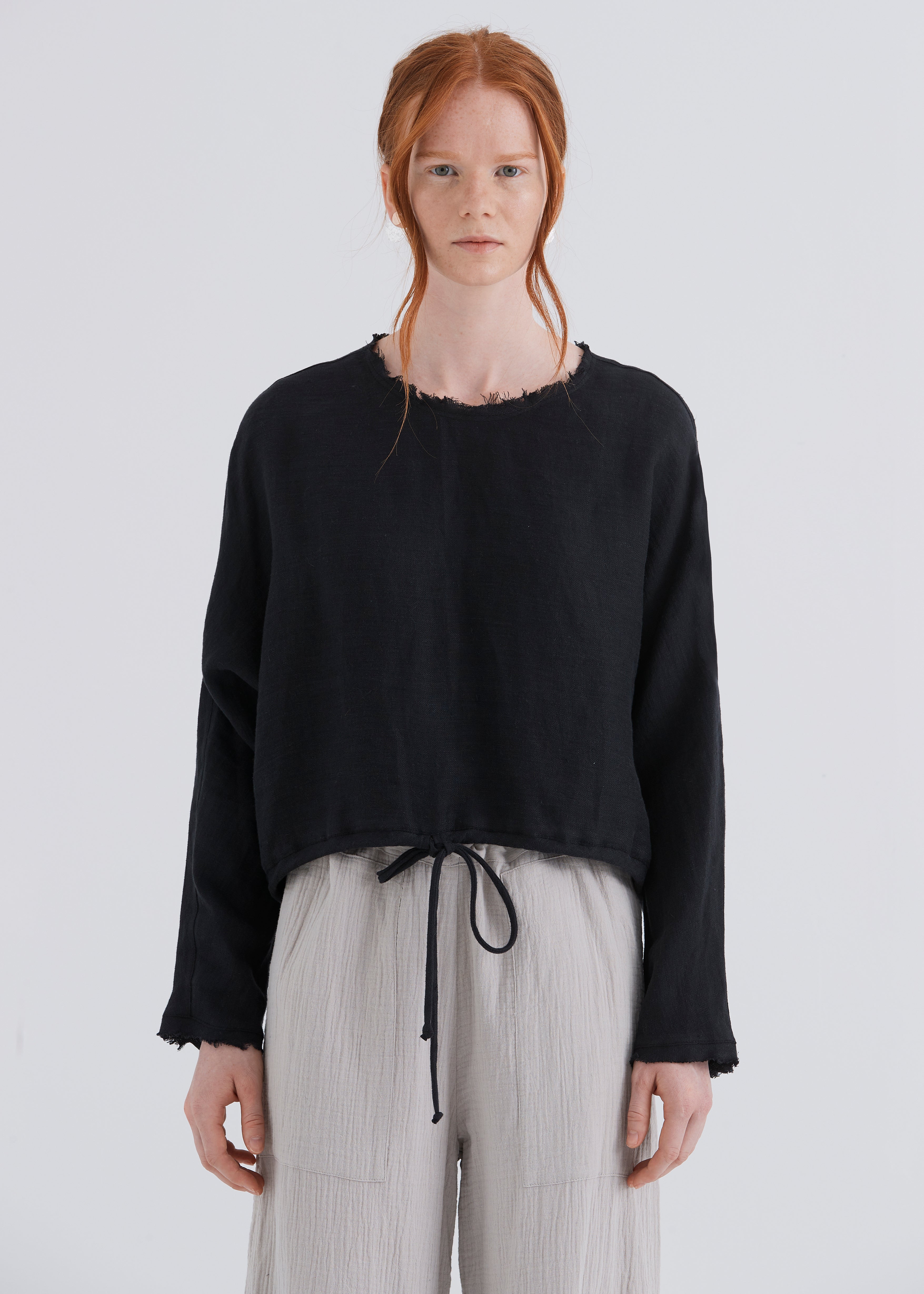 Person wearing a black sweater and light gray pants on a white background