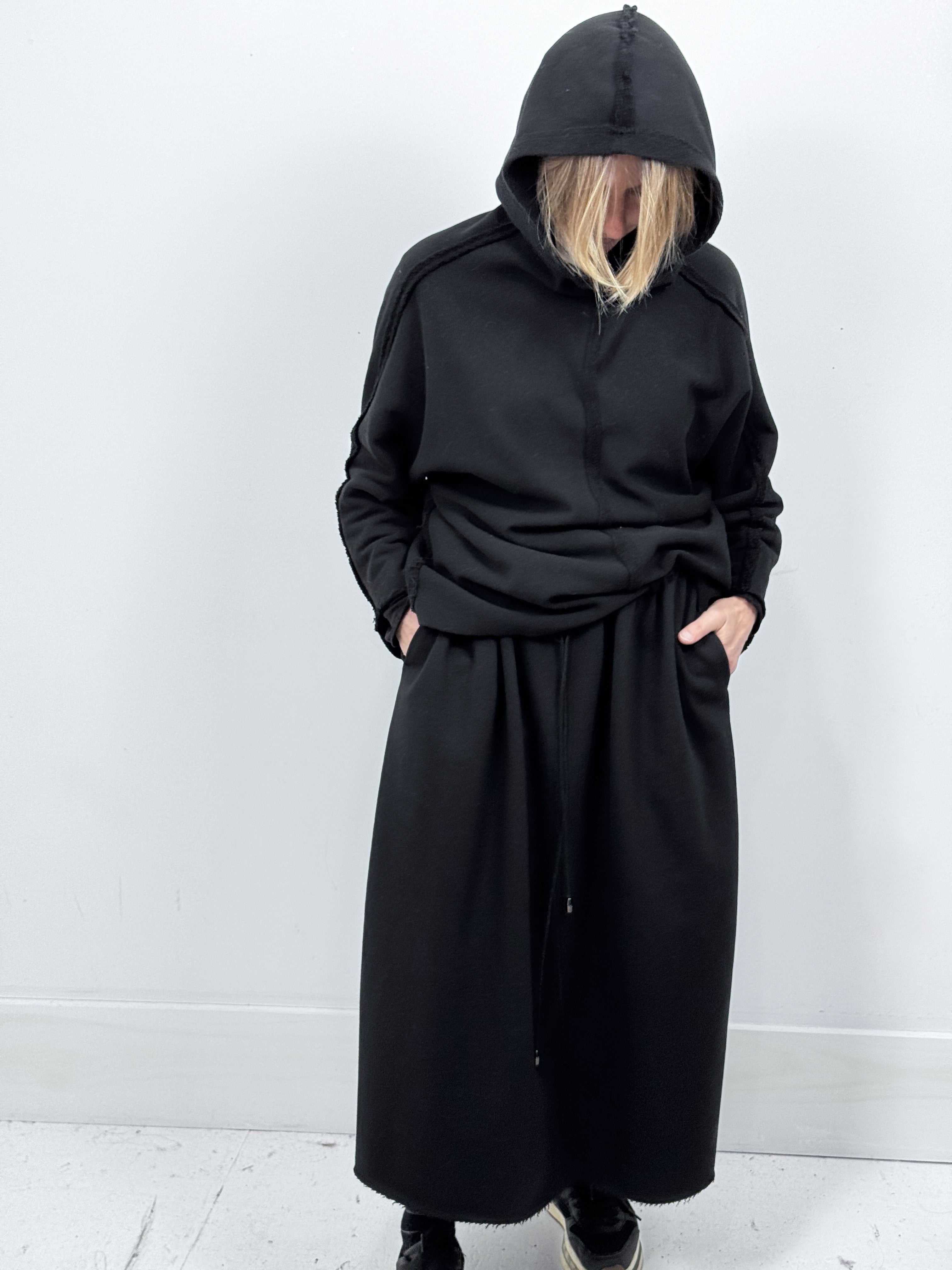 Woman wearing a long black hooded coat against a white background