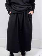 Person wearing a long black coat against a plain background