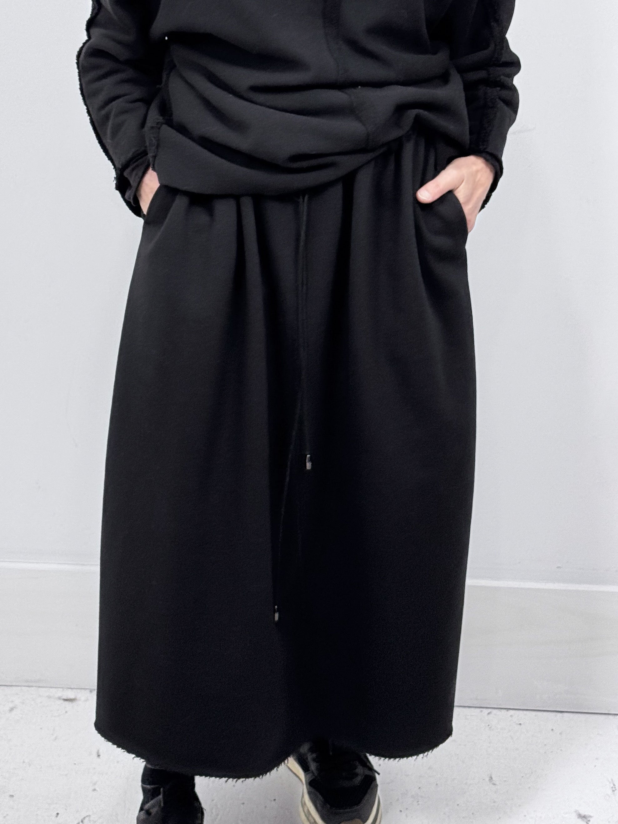 Person wearing a long black coat against a plain background