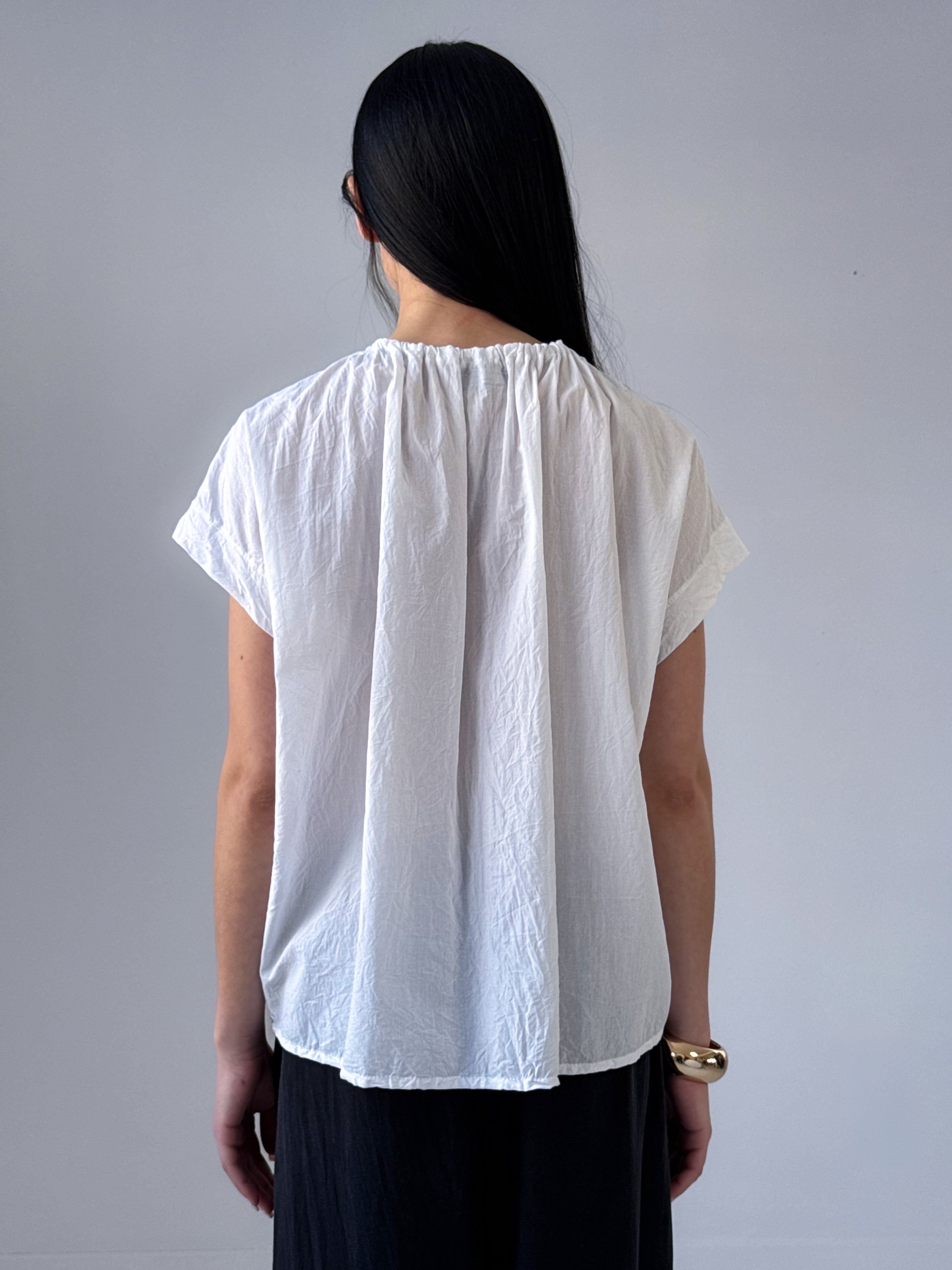 Person wearing a white blouse with short sleeves against a gray background