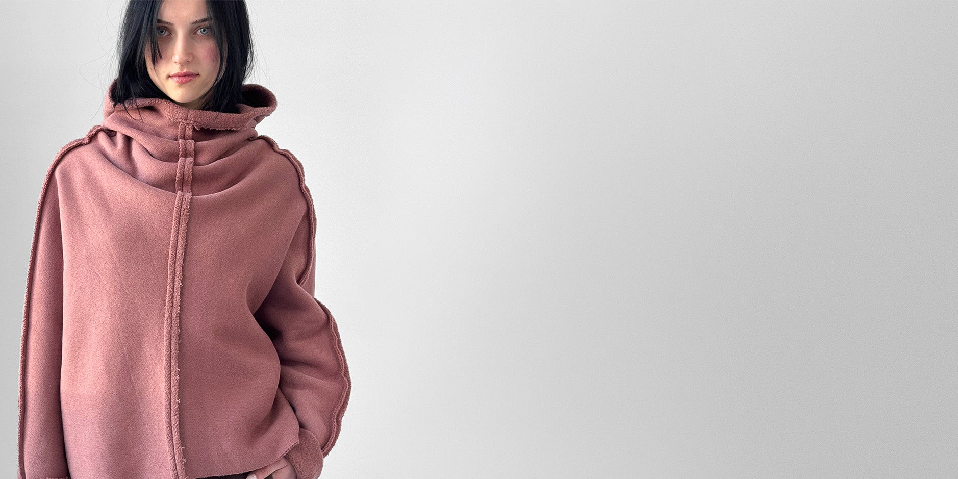 Person wearing a pink hooded sweater on a plain background