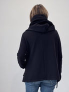 Person wearing a black jacket with a hood on a plain background