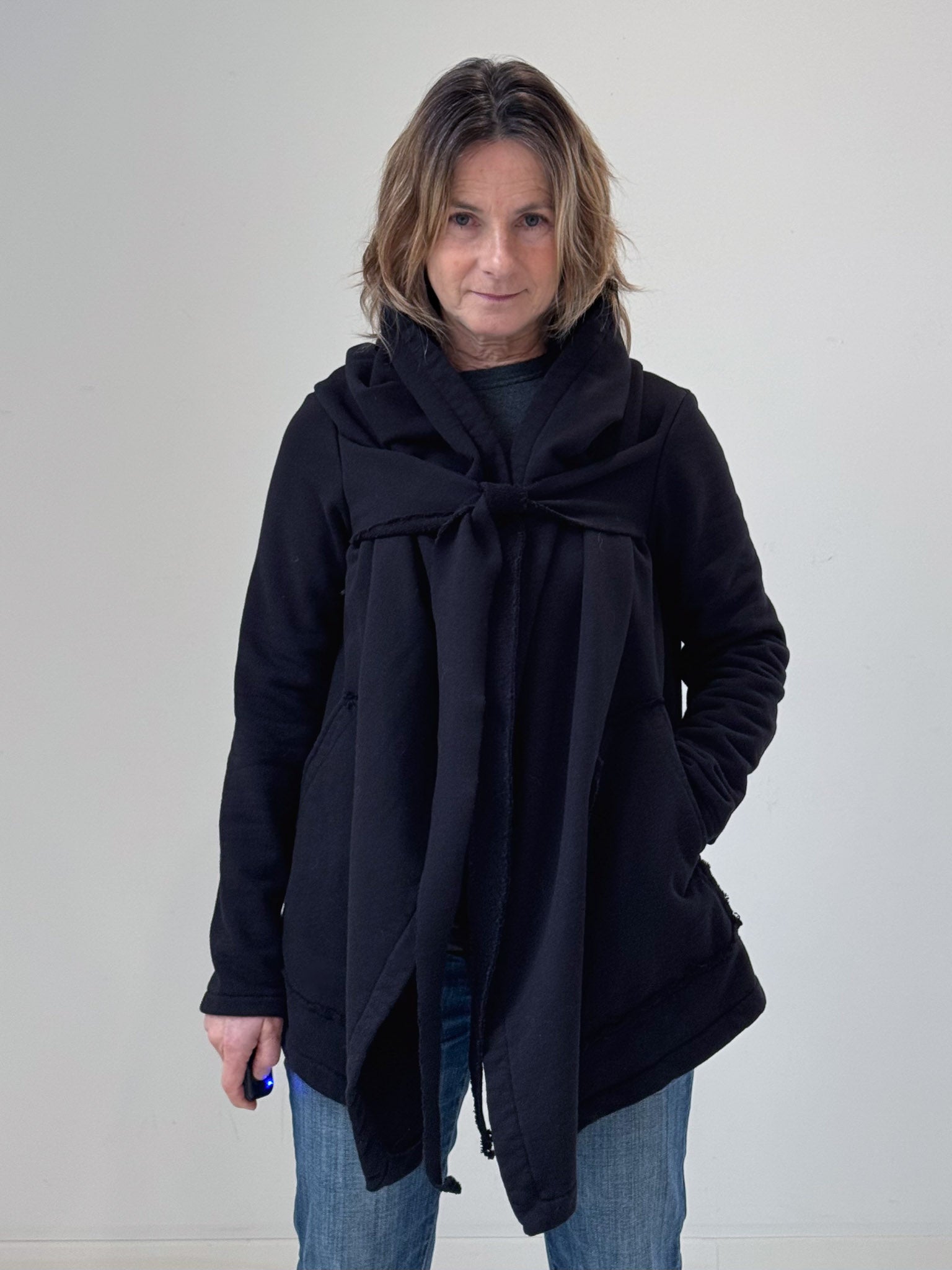 Woman wearing a black coat with a large scarf against a plain background