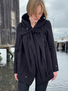 Person wearing a black coat with a bow detail outdoors on a snowy day.