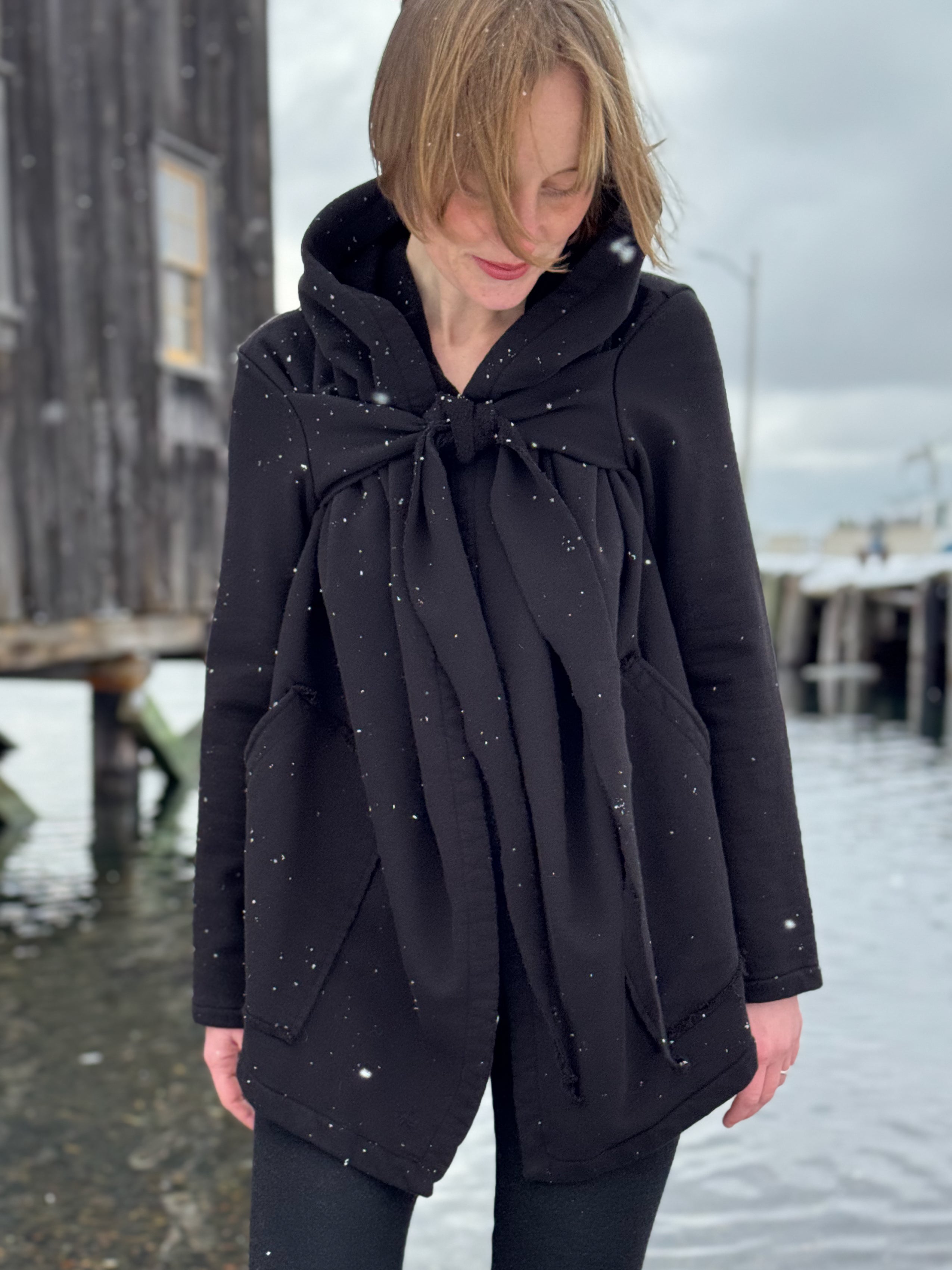 Person wearing a black coat with a bow detail outdoors on a snowy day.