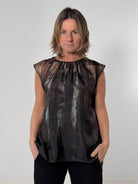 Person wearing a sleeveless black and brown patterned top against a plain background