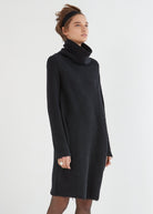 A model wearing a black, loosely draped pullover dress with a large neckline and long sleeves.