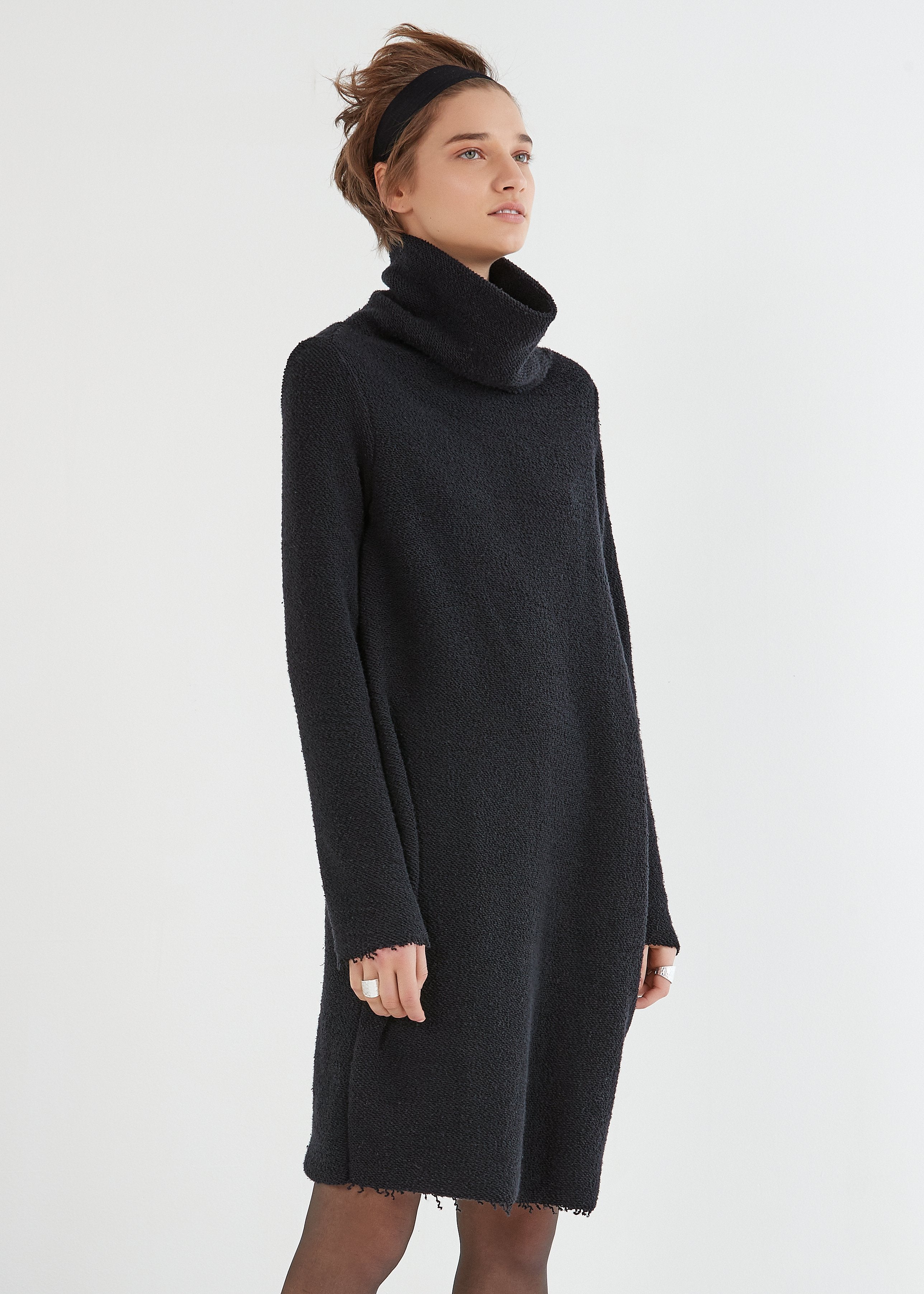 A model wearing a black, loosely draped pullover dress with a large neckline and long sleeves.